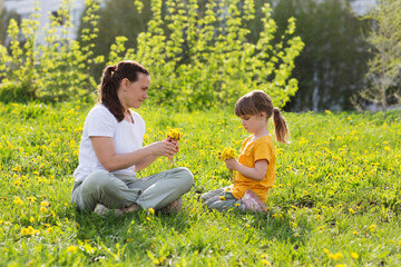 mom and little daughter sitting on the grass with flowering dandelions in spring. stress relief. Spring awakening. Slow life. Enjoying the little things. Dreaming of spring. 