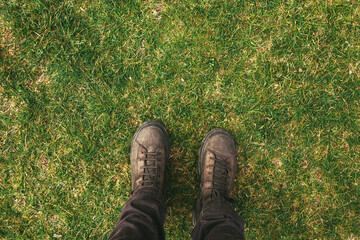 Top view of male feet in boots standing on green grass lawn