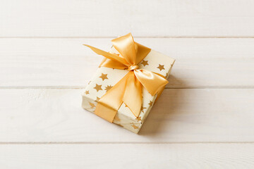 wrapped Christmas or other holiday handmade present in white paper with gold ribbon on colored background. Present box, decoration of gift on colored table, top view with copy space