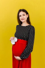Happy pregnant woman holding baby girl booties against her belly at Colored background. Happy pregnancy. Copy space