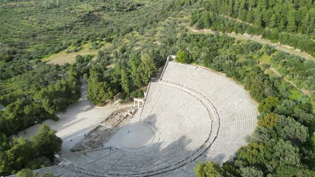 Aerial drone shot of the Epidaurus Theatre in Greece, showcasing its grand scale of theatre compared to a person at its center, surrounded by trees.