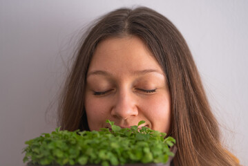 A woman with closed eyes and a serene expression inhales deeply the fresh scent of vibrant microgreens, suggesting a moment of connection with nature. 
