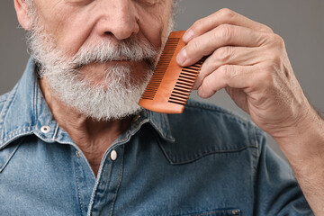 Man combing beard on grey background, closeup