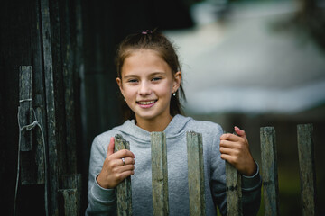 A teenage girl stands behind a wooden fence, her gaze directed forward, she looks contemplative and dreamy. - 785096138