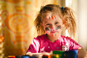 A girl with paints, her face painted in bright colors, her expression full of delight and joy. - 785096141