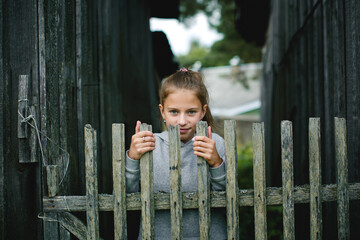 A teenage girl by a wooden fence, her face expressing quiet determination and tenderness. - 785096149
