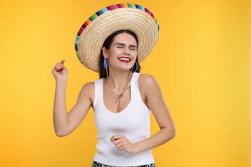 Young woman in Mexican sombrero hat dancing on yellow background