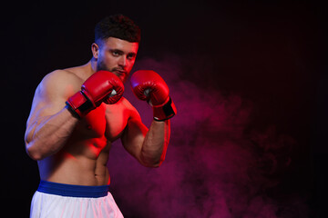 Man wearing boxing gloves on dark background. Space for text