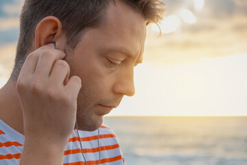 Portrait of Caucasian young man wearing earphones on the sea coast and listening to music. Handsome...