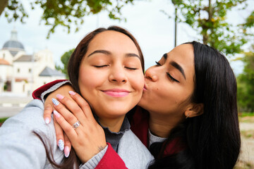 Happy Latin lesbian couple kissing and taking a selfie at street. LGBT couple.