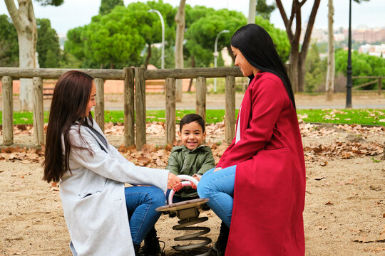 Latin lesbian couple playing with their son in the children's playground. LGBT family.