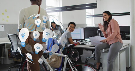 Image of globe of lightbulbs over diverse business people with bicycle greeting in office