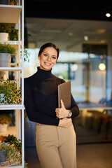 Portrait of a smiling businesswoman, holding a laptop, posing for the camera. - 785105354