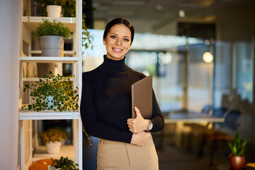 Portrait of a smiling businesswoman, dressed elegantly, holding a laptop in her hands.