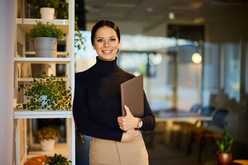 Portrait of a smiling businesswoman, posing for the camera, holding a laptop.