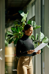 An elegant businesswoman reading one document, standing by the window on a sunny day. - 785106786