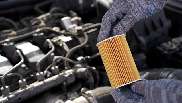 Auto mechanic changes oil filter for diesel cars, holds new oil filter in his hands against background engine compartment, close-up. Concept replacing auto parts, servicing car in car service center. 