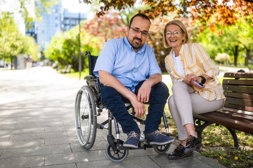 Man in wheelchair is spending time with his mother in park. - 785111141