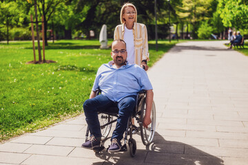 Man in wheelchair is spending time with his mother in park. They are enjoying sunny day together. - 785111500