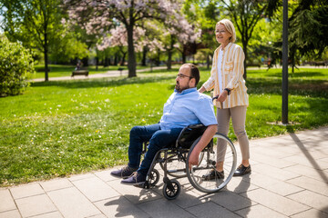Man in wheelchair is spending time with his mother in park. They are enjoying sunny day together. - 785111524