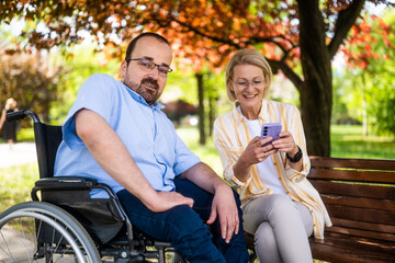 Man in wheelchair is spending time with his mother in park. - 785111547