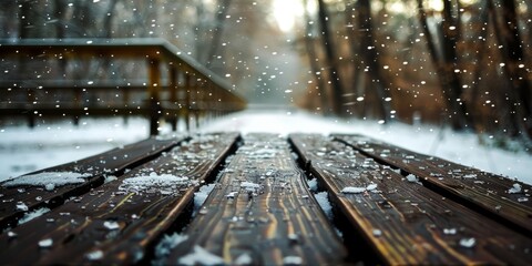 Winter scene with snowflakes falling on a rustic wooden footbridge in a tranquil forest.