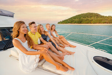 Friendship and vacation. Group of laughing young people sitting on the yacht deck sailing the sea sunset