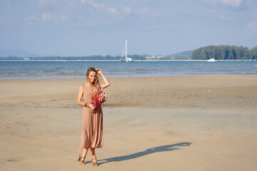 Young beautiful woman holding bouquet on tropical beach in Thailand