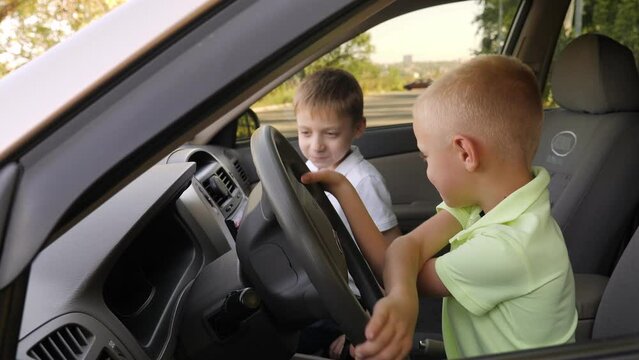 Close-up of a little boy and his brother sitting in the car behind the wheel and playing, the boy honks and turns the steering wheel.