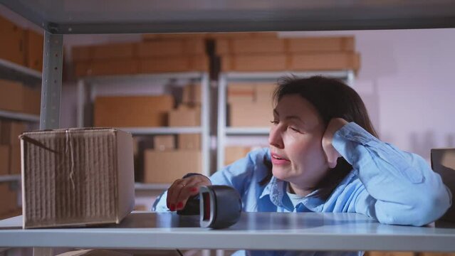 A sleepy and tired woman at work in a box warehouse