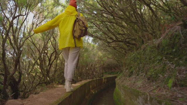 A girl in a yellow jacket travels with a backpack and visits extraordinary places and trails on the island of Madeira, Levada dos Tornos, Portugal