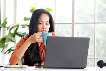 Happy asian women working online with laptop computer at home office, Asia female smiling and holding coffee cup while relaxing from working - 785120392