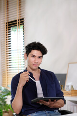 Portrait of happy young business man owner holding digital tablet smiling and looking at camera while sitting at home office - 785120563