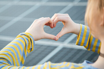 Young girl staying near solar panels and showing heart symbol. Solar energy concept. Renewable...