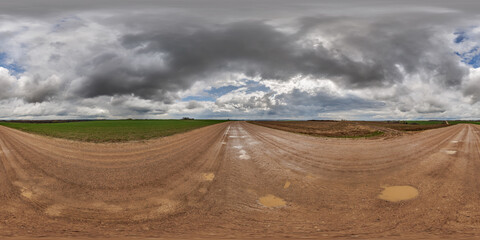 hdri 360 panorama on wet gravel road with puddles among fields in spring nasty day with storm clouds in equirectangular full seamless spherical projection, for VR AR virtual reality content