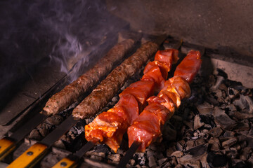 Close-up of an appetizing kebab or shashlik made of fresh meat and lula kebab is cooked on a charcoal grill with smoke.