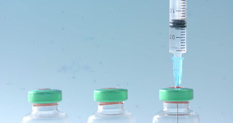 Syringe in the first of a row of vaccine vials on blue background