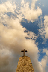 silhouette of stone grave cross against the background of a blue evening sky with clouds