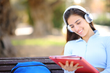 Happy student in a park listening audio guide and reading notes