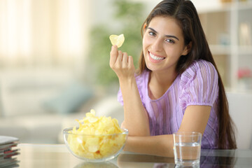 Happy woman looks at you holding potato chip