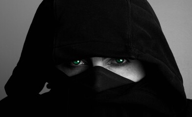 Closeup portrait of bright green eyes of a person covered with black hijab in grayscale