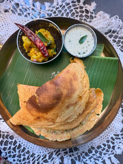 Masala dosa, a south Indian traditional and popular crepe with filling of a mixture of mashed potatoes and fried onions served with chutney and sambar over a white cloth background, 