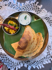 Masala dosa, a south Indian traditional and popular crepe with filling of a mixture of mashed potatoes and fried onions served with chutney and sambar over a white cloth background, 
