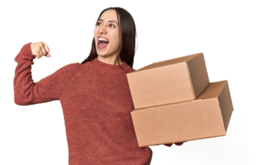 Caucasian young woman with moving boxes on studio background raising fist after a victory, winner concept.