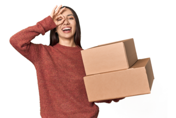 Caucasian young woman with moving boxes on studio background excited keeping ok gesture on eye.