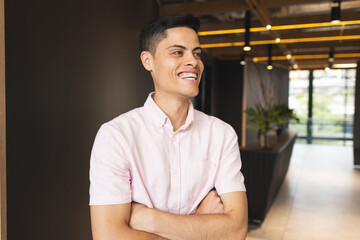 A biracial young man wearing a pink shirt is standing, arms crossed, laughing
