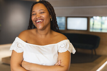 A biracial young woman wearing a white off-shoulder top is laughing in a modern business office