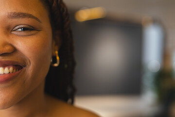 Young biracial woman smiling, wearing gold hoop earrings in a modern business office with copy space