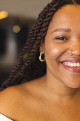 A young biracial woman is smiling, wearing nose ring and hoop earrings, in a modern business office