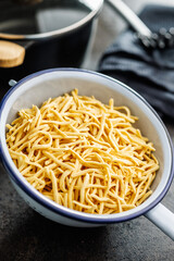 Uncooked spaetzle pasta in colander on kitchen table.